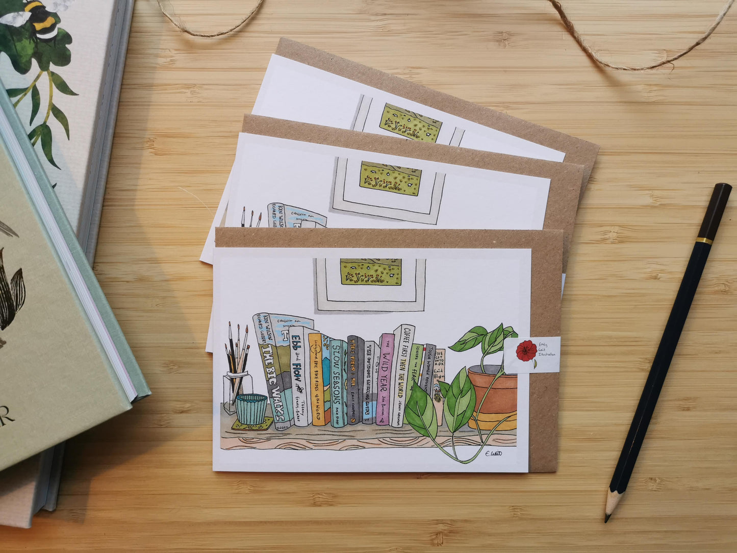 Set of greeting cards with illustrations of books on a bookshelf. The cards are on a wooden surface with a pencil.