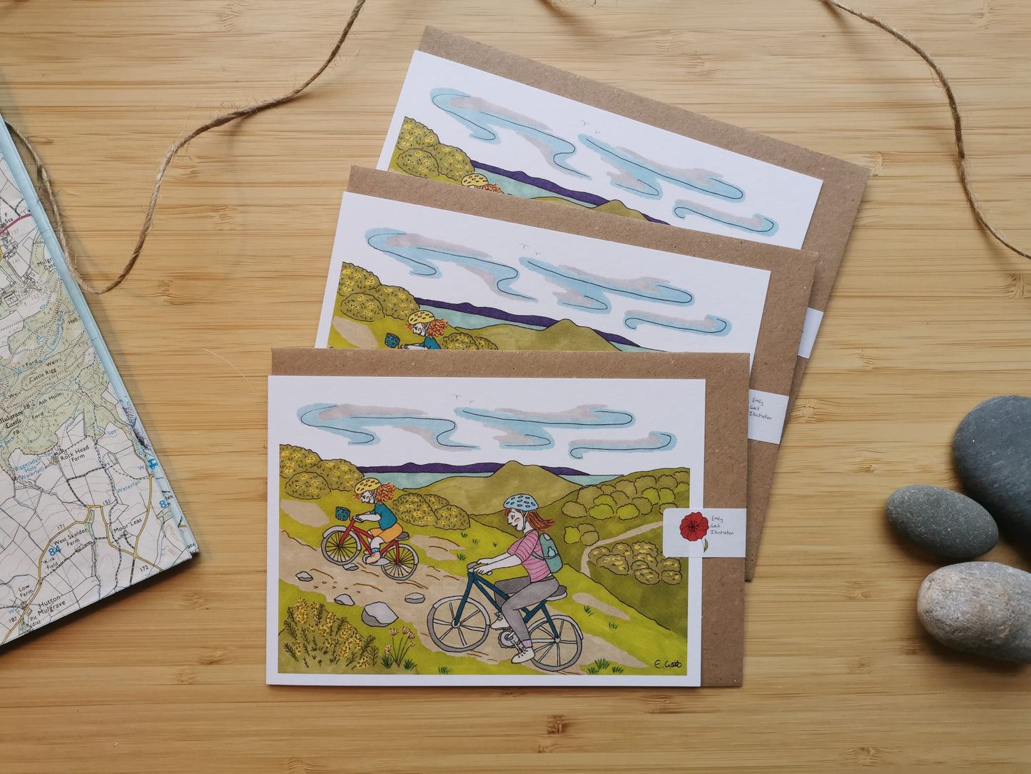 Set of greeting cards with bicycle-themed illustrations of a mother and her daughter cycling up hill with Edinburgh, Arthur's Seat and the sea in the background.