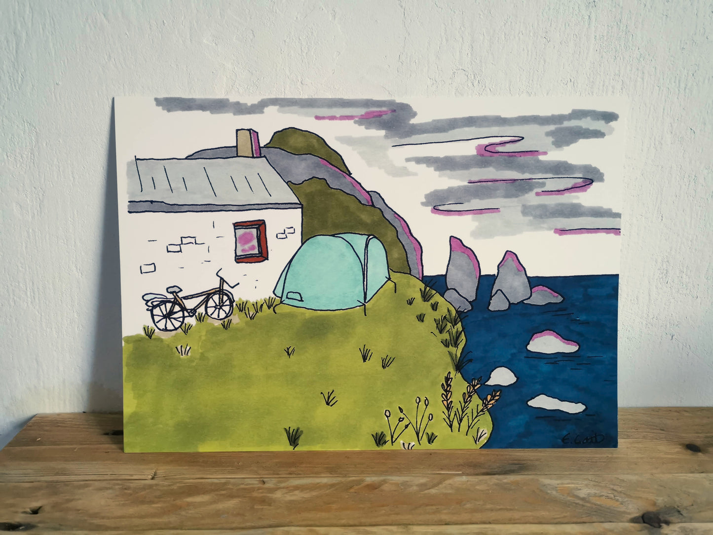 Hand-drawn landscape with a house, tent, and bicycle on a wooden surface.