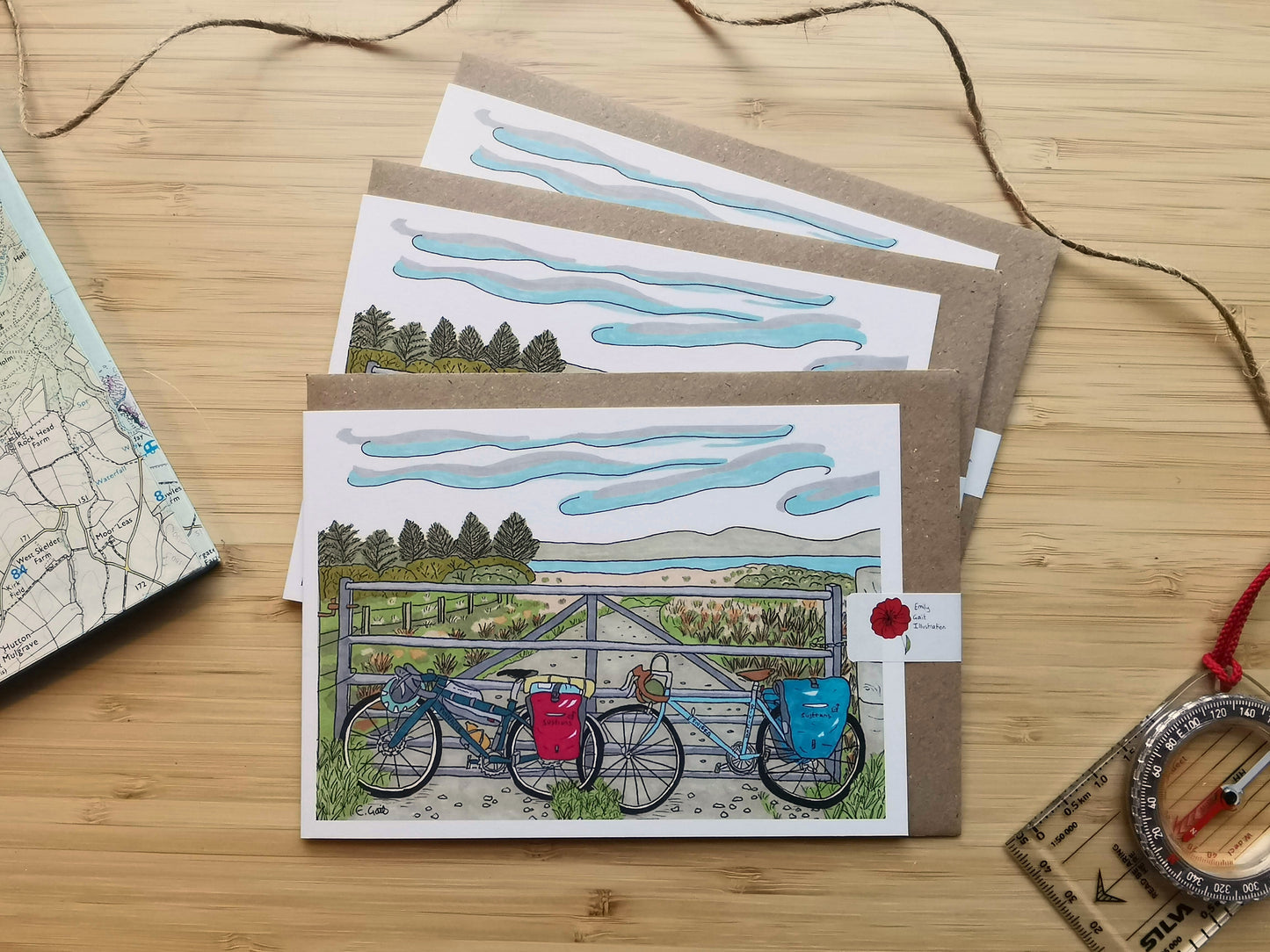 Set of 3 illustrated greeting cards of two bikes packed up for a camping trip with a view of the sea and hills in the background.
