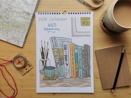 2026 calendar titled 'Wild Adventures' on a wooden surface with a map, coffee cup, and notebook.