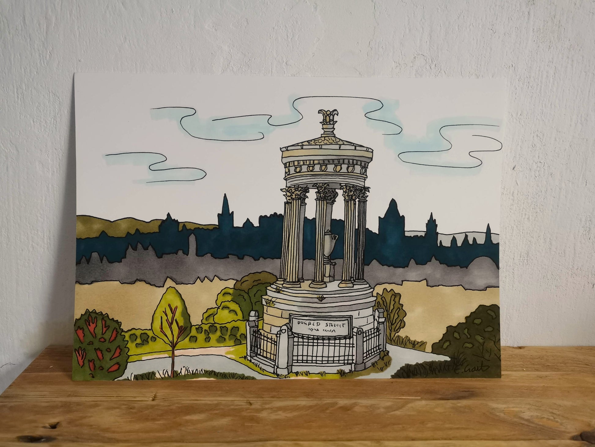 Illustration of a monument on top of Calton Hill with the cityscape of Edinburgh in the background on a wooden surface.