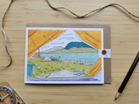 Card with a scenic illustration of looking out of a tent onto a loch with a bicycle parked up, on a wooden surface with a pen and string.