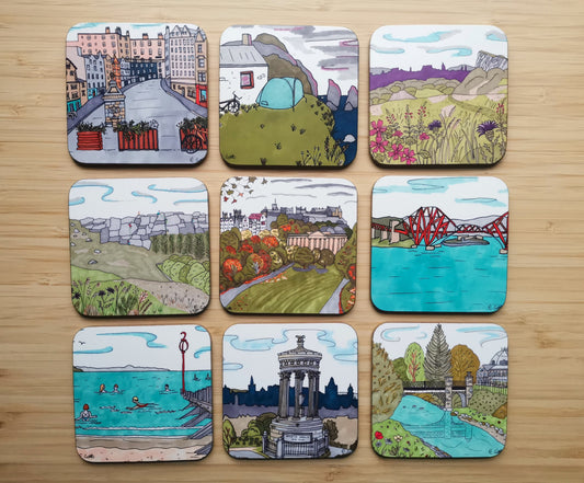 Set of 9 illustrated coasters on a wooden surface. The designs include Victoria Street in Edinburgh, Camping next to the sea, Arthur's Seat, Climbing on Stanage Edge, an Autumn park scene in Edinburgh, Forth Rail Bridge, people swimming on the beach, a view from Calton Hill with Edinburh in the background and a park scene with Buxton Pavilion in the background.