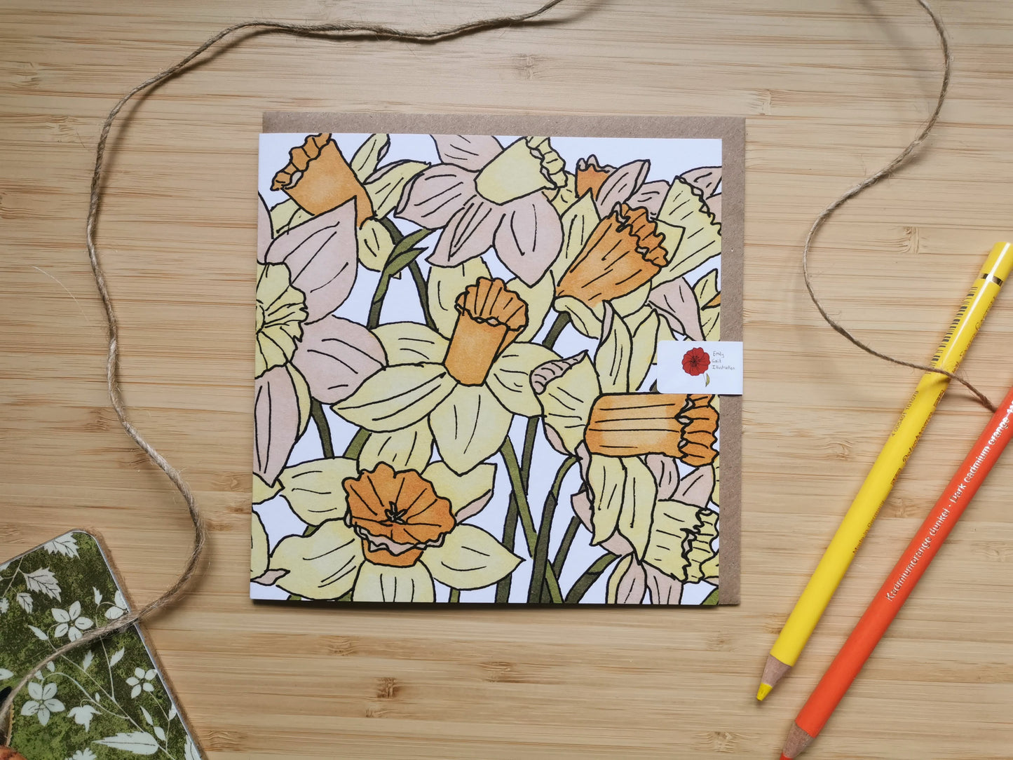 Floral card of a daffodil design on a wooden surface with colored pencils