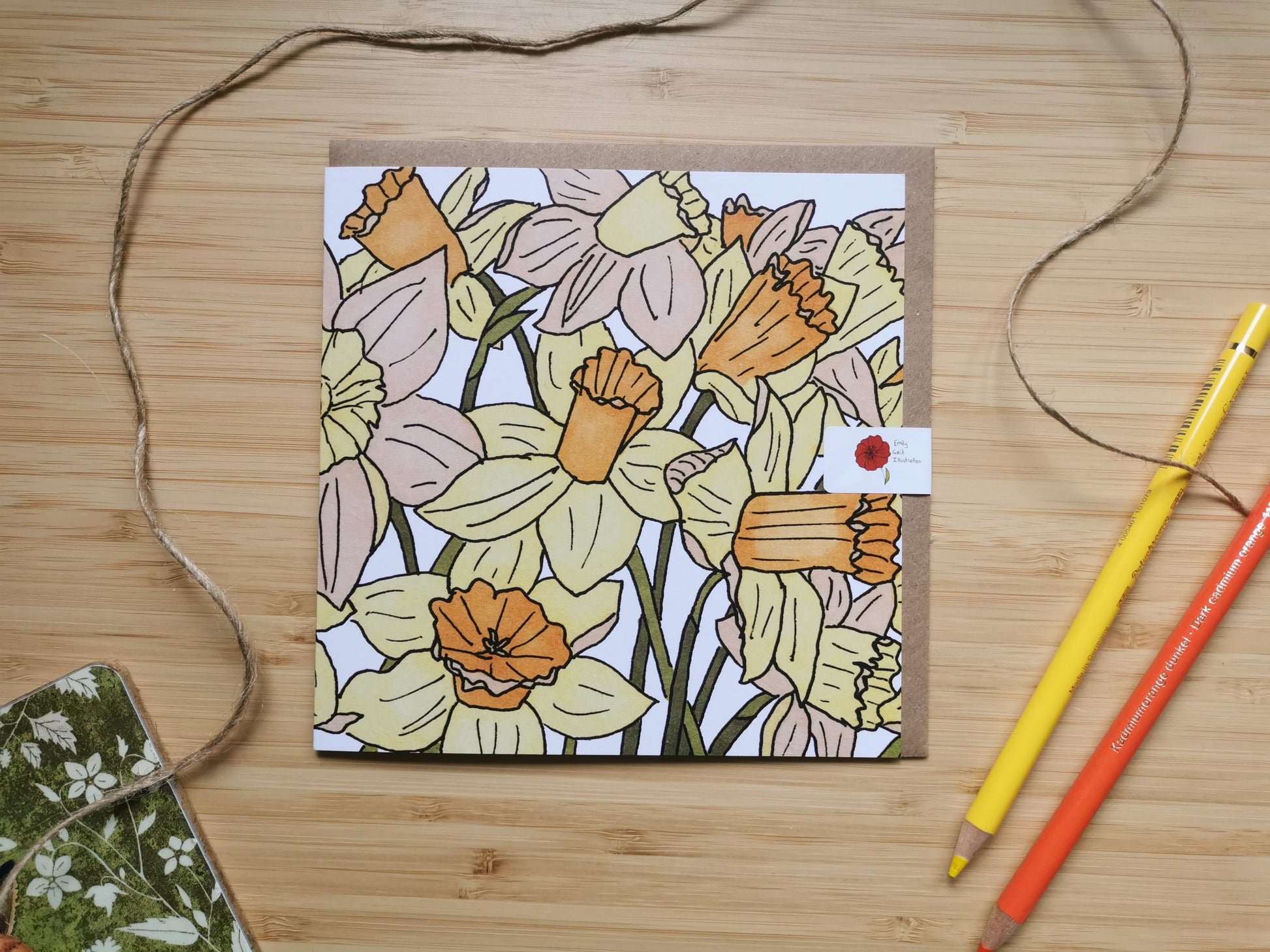 Floral card of a daffodil design on a wooden surface with colored pencils