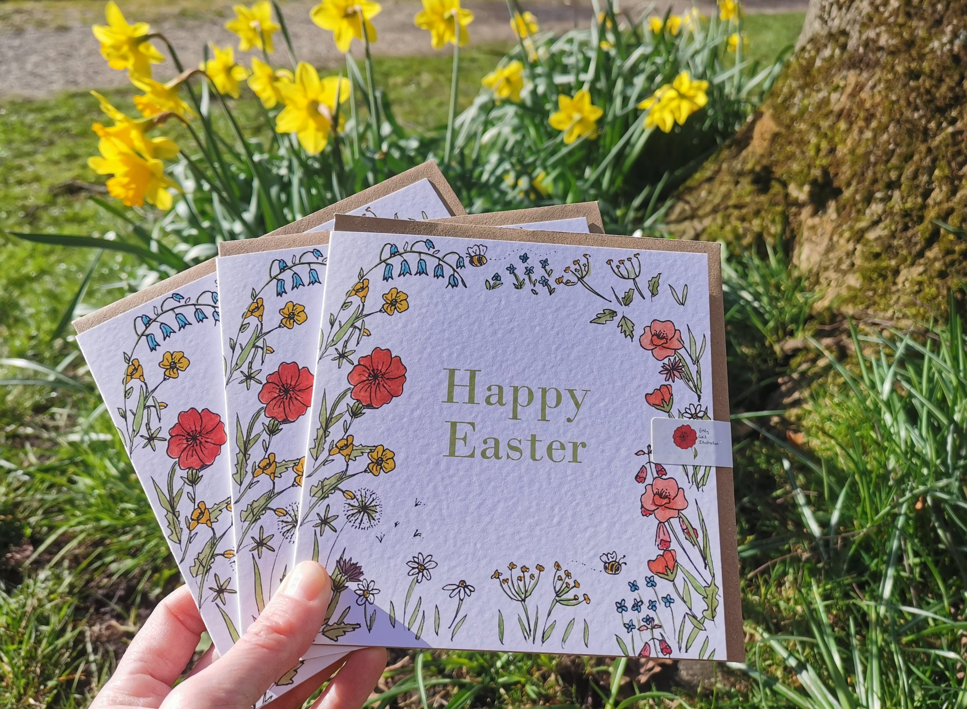 Three Easter greeting cards with floral designs held in front of daffodils.