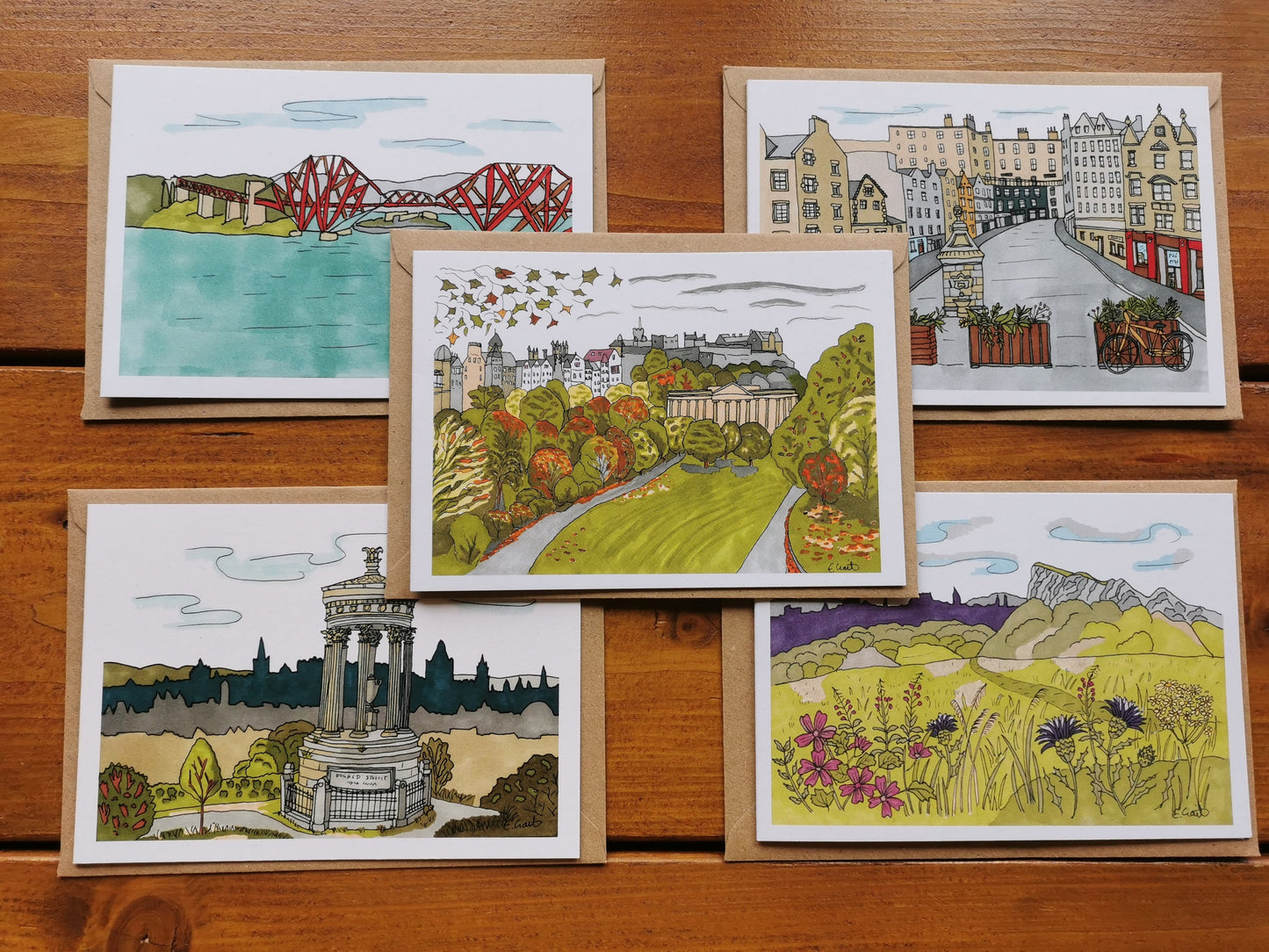 A set of five greeting cards featuring pen and ink illustrations of Edinburgh, Scotland, including iconic scenes like the Forth Rail Bridge and Salisbury Crags, displayed on a wooden surface.