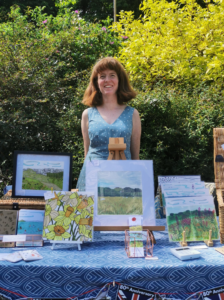 Woman standing behind a table displaying artwork outdoors