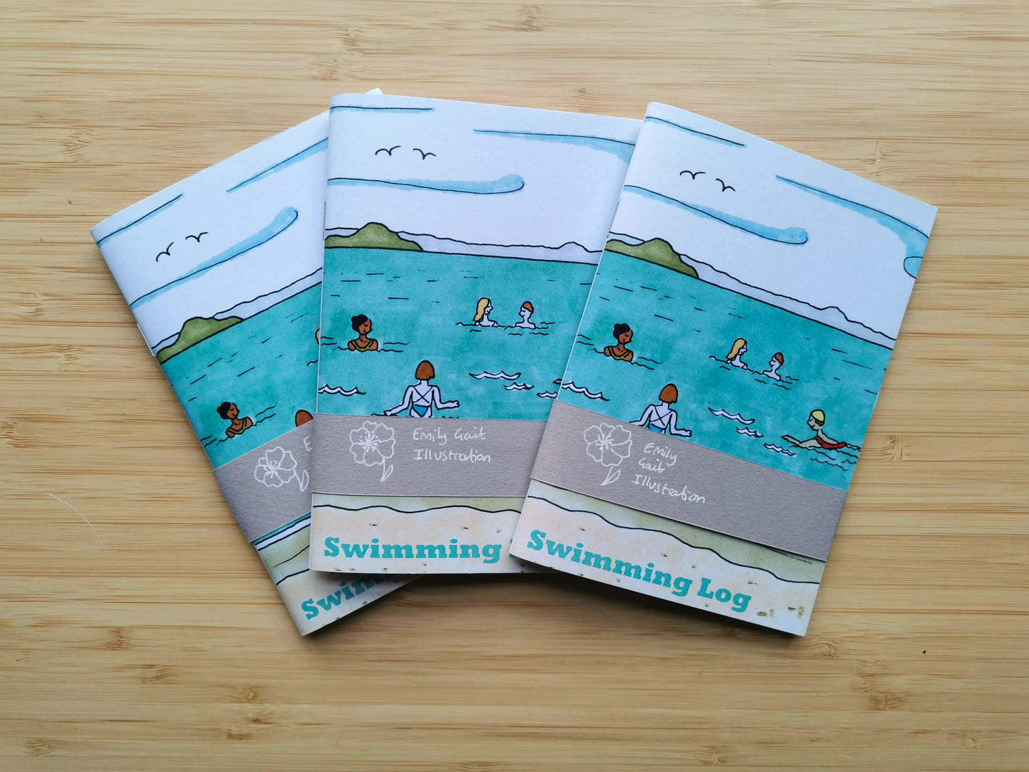 Three swimming log books with illustrations of people swimming on a wooden surface