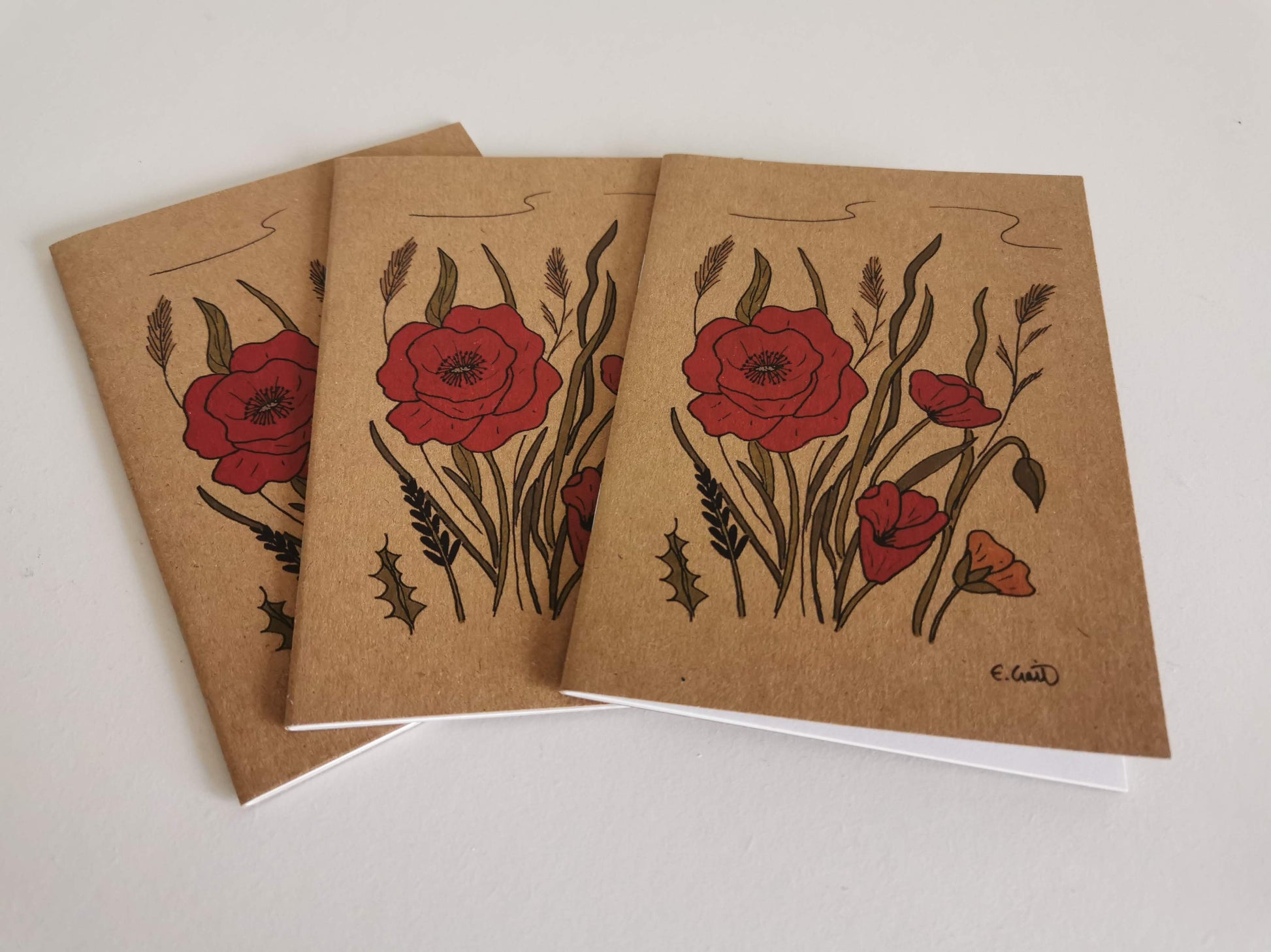 A stack of A6 size notebooks with a illustration of red wild poppies on the cover.